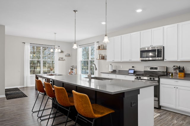 kitchen with dark wood finished floors, a center island with sink, appliances with stainless steel finishes, white cabinetry, and a sink