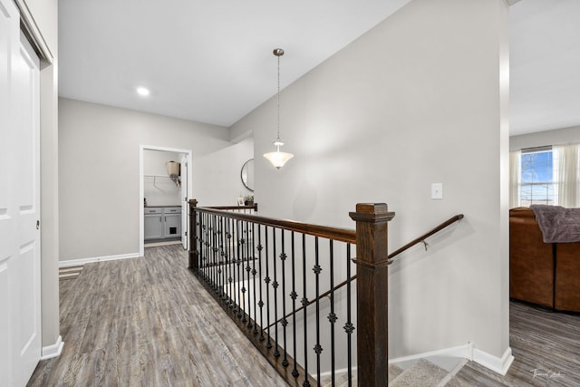 hallway with baseboards, wood finished floors, and an upstairs landing