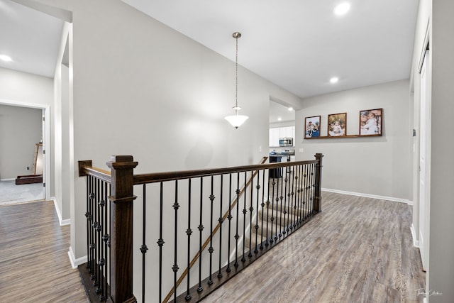 hallway featuring wood finished floors, an upstairs landing, and baseboards