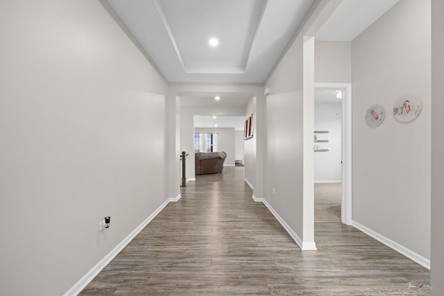 hallway featuring a tray ceiling, recessed lighting, wood finished floors, and baseboards