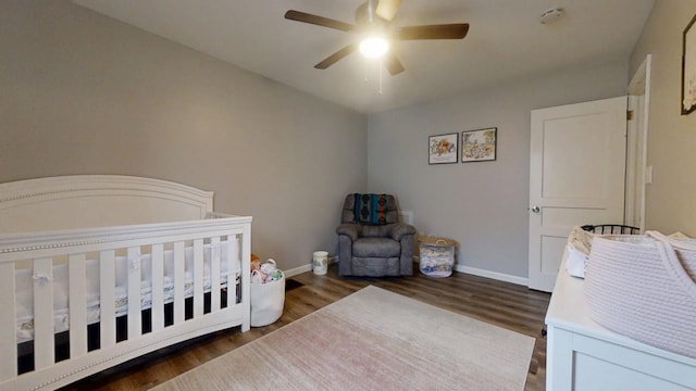 bedroom featuring a crib, dark wood-type flooring, and ceiling fan