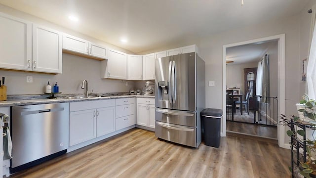 kitchen with appliances with stainless steel finishes, sink, white cabinets, and light hardwood / wood-style floors