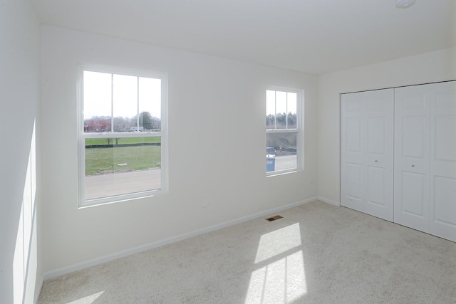 unfurnished bedroom with light carpet, multiple windows, and a closet