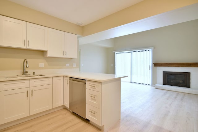 kitchen with a fireplace, white cabinetry, dishwasher, sink, and kitchen peninsula