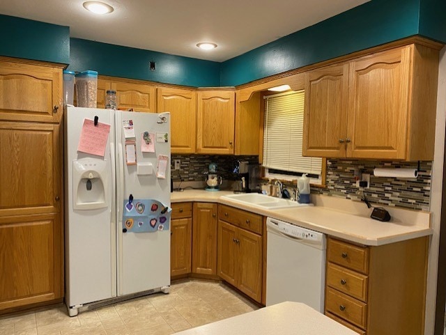 kitchen with white appliances, tasteful backsplash, brown cabinets, light countertops, and a sink