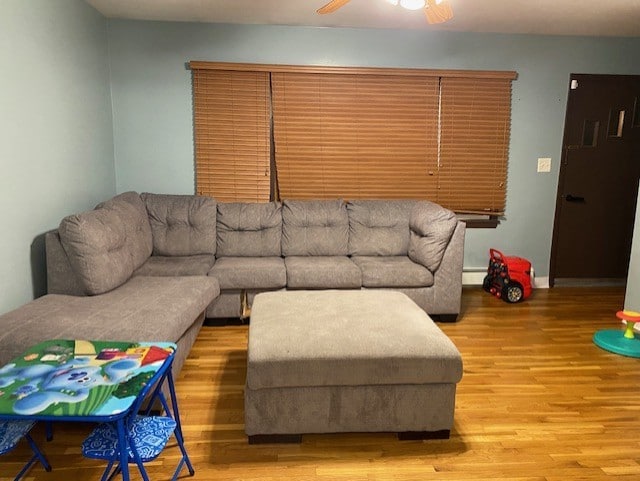 living area with baseboard heating, wood finished floors, a ceiling fan, and baseboards