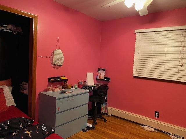 bedroom featuring a baseboard heating unit, ceiling fan, wood finished floors, and baseboards