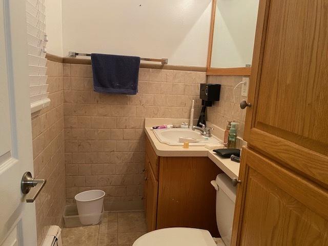 half bath with toilet, tile patterned flooring, tile walls, and vanity