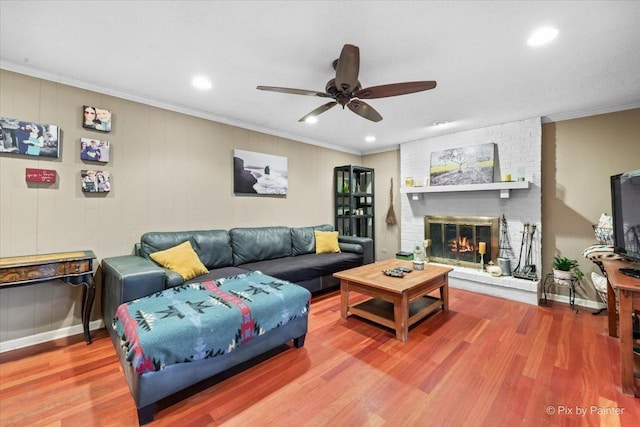 living room with wood-type flooring, a brick fireplace, ornamental molding, and ceiling fan