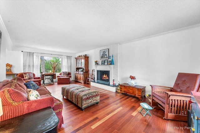 living room with hardwood / wood-style flooring, ornamental molding, a brick fireplace, and a textured ceiling