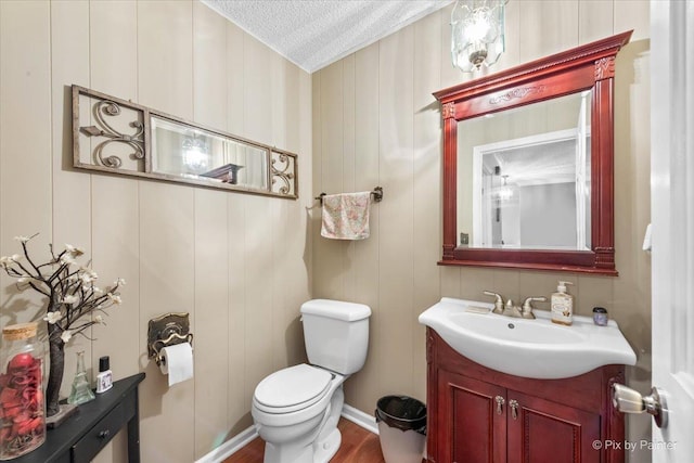 bathroom featuring hardwood / wood-style floors, wooden walls, vanity, toilet, and a textured ceiling