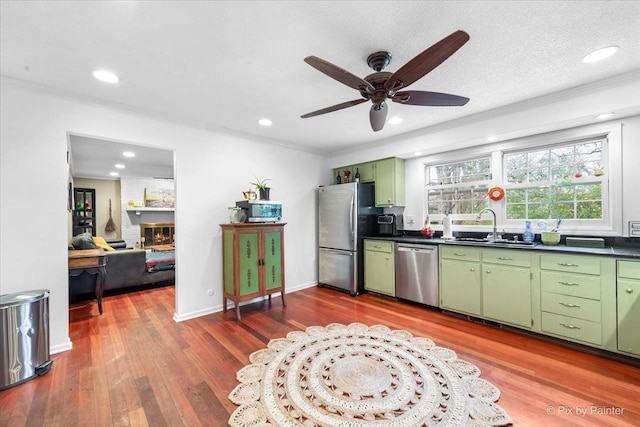 kitchen with sink, ceiling fan, stainless steel appliances, green cabinetry, and a brick fireplace