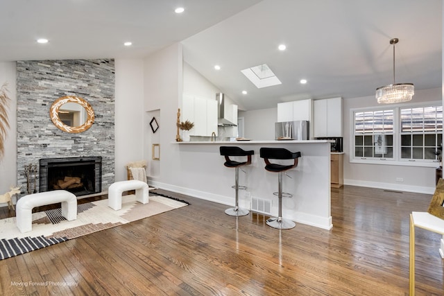 kitchen featuring a stone fireplace, a breakfast bar area, visible vents, wall chimney range hood, and freestanding refrigerator