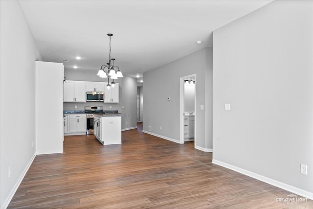 kitchen with appliances with stainless steel finishes, decorative light fixtures, white cabinets, hardwood / wood-style flooring, and a center island