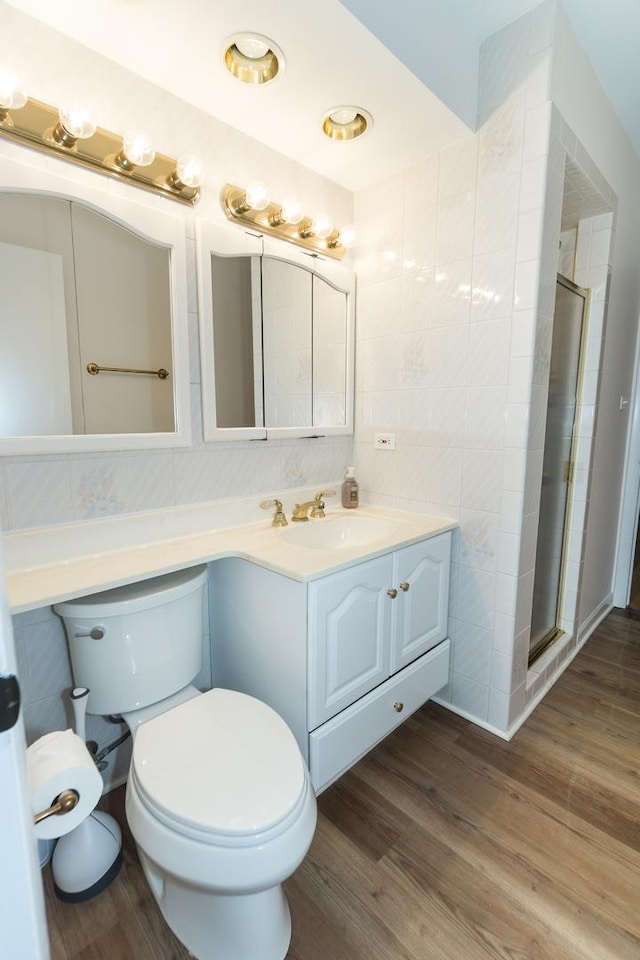 bathroom with toilet, a shower with shower door, tile walls, vanity, and hardwood / wood-style floors