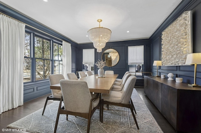 dining space featuring a notable chandelier, ornamental molding, a decorative wall, and dark wood-type flooring