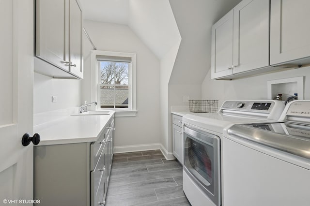 laundry room featuring washer and clothes dryer, baseboards, a sink, cabinet space, and wood tiled floor