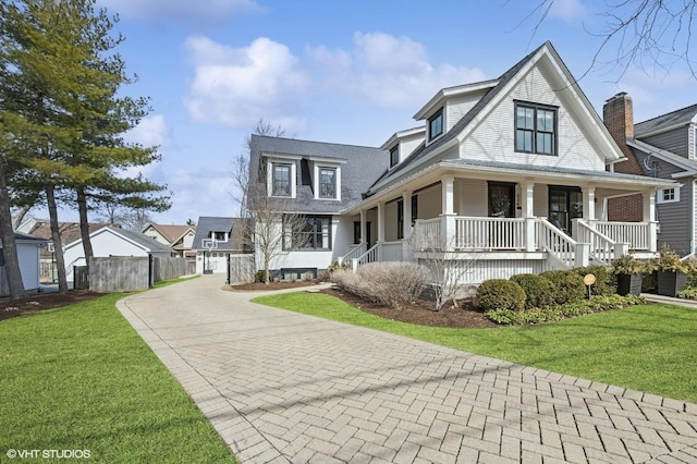 view of front of house featuring covered porch, fence, a front yard, and decorative driveway