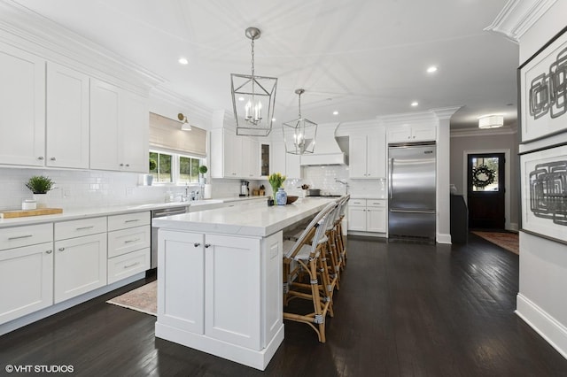 kitchen with white cabinets, ornamental molding, stainless steel appliances, custom range hood, and a center island