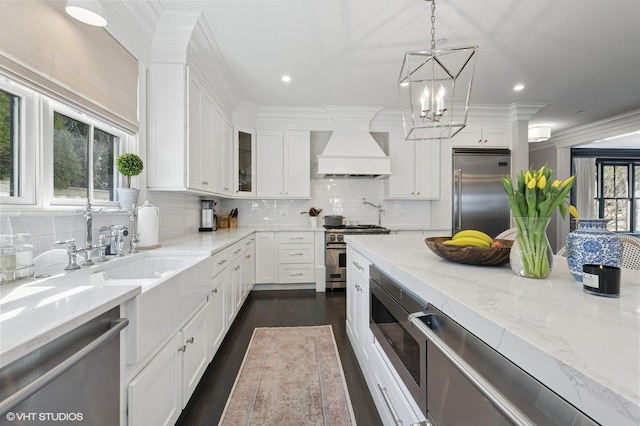 kitchen with built in appliances, tasteful backsplash, premium range hood, white cabinets, and ornamental molding