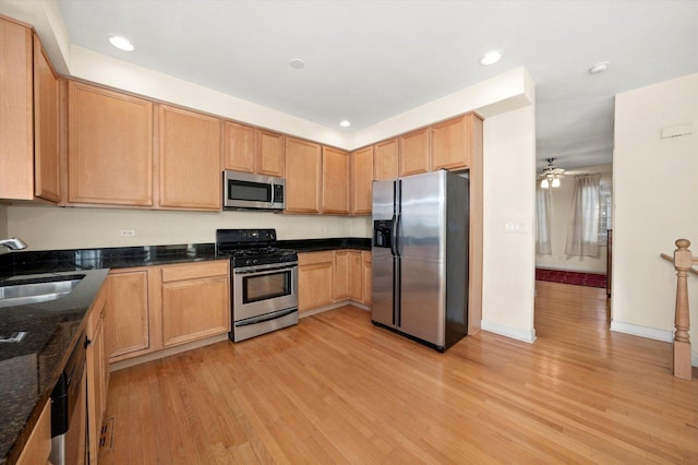 kitchen with appliances with stainless steel finishes, sink, light hardwood / wood-style flooring, and dark stone countertops