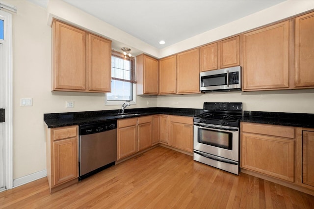 kitchen with stainless steel appliances, sink, dark stone countertops, and light hardwood / wood-style floors