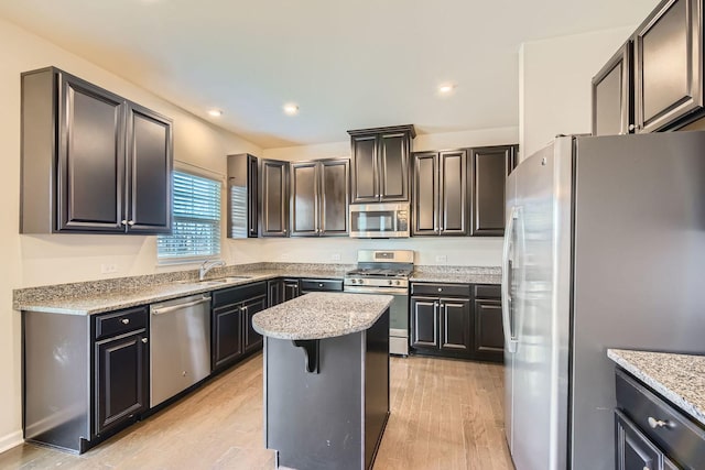 kitchen with sink, light stone counters, light wood-type flooring, a kitchen island, and stainless steel appliances