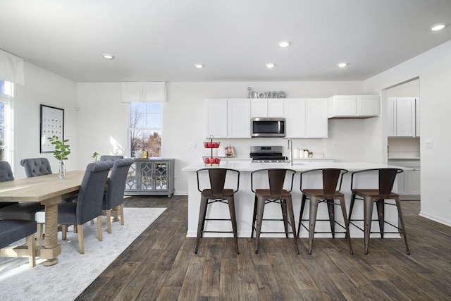 kitchen with a breakfast bar, appliances with stainless steel finishes, dark hardwood / wood-style floors, an island with sink, and white cabinets