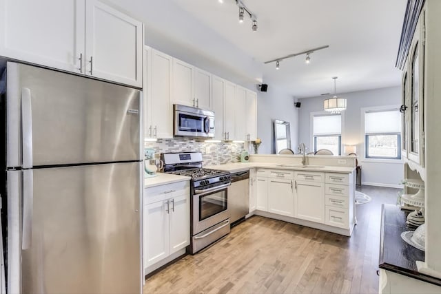 kitchen with stainless steel appliances, a peninsula, a sink, white cabinets, and tasteful backsplash