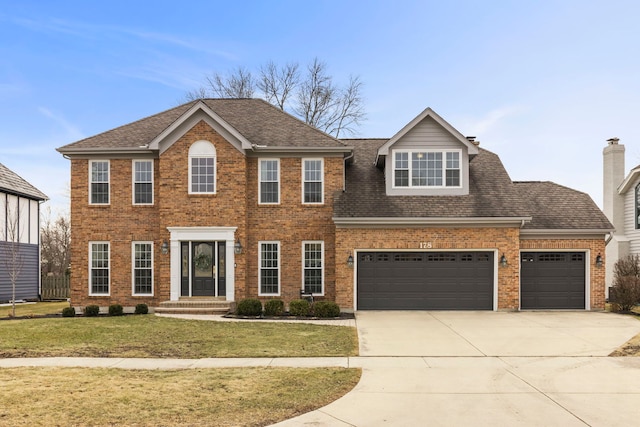 colonial home with an attached garage, a front lawn, concrete driveway, and brick siding