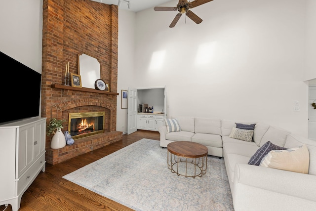 living room with a ceiling fan, dark wood-style flooring, a fireplace, and a high ceiling