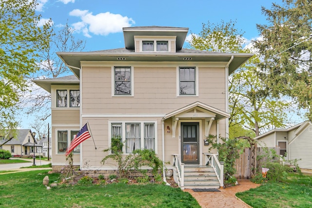 american foursquare style home featuring a shingled roof and a front lawn