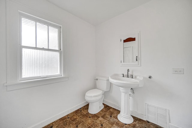 half bath with toilet, baseboards, visible vents, and a healthy amount of sunlight