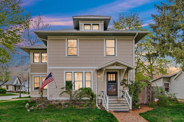 american foursquare style home featuring roof with shingles and a front yard