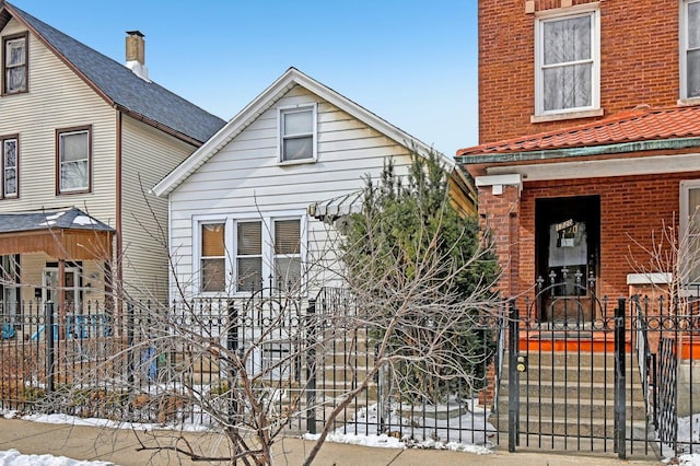 view of snowy exterior featuring a fenced front yard, a gate, and brick siding