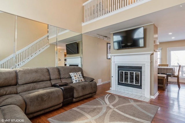 living room with a tiled fireplace, rail lighting, a high ceiling, and dark hardwood / wood-style flooring