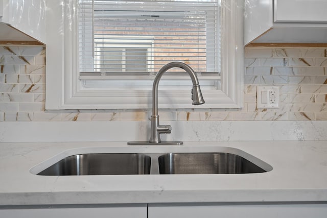 interior details with white cabinetry, light stone countertops, sink, and tasteful backsplash