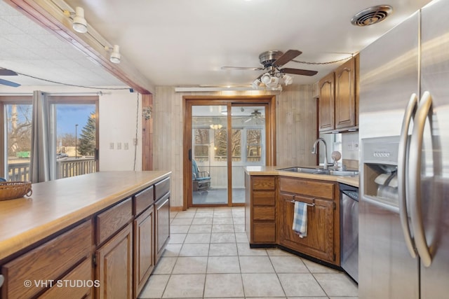 kitchen with appliances with stainless steel finishes, wooden walls, sink, light tile patterned floors, and ceiling fan