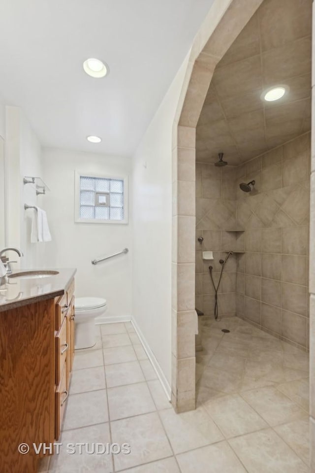 bathroom with a tile shower, vanity, tile patterned flooring, and toilet