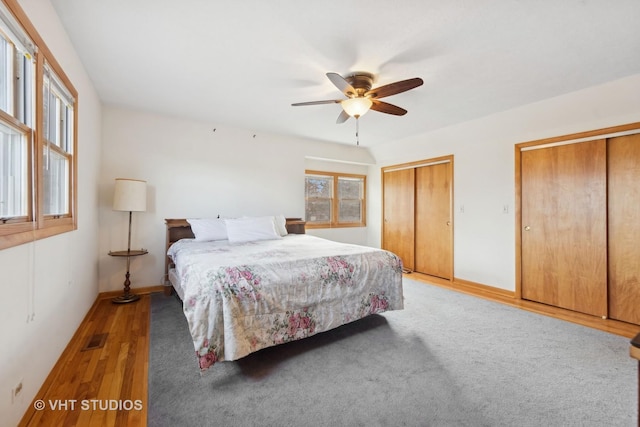 bedroom with hardwood / wood-style flooring, ceiling fan, and two closets