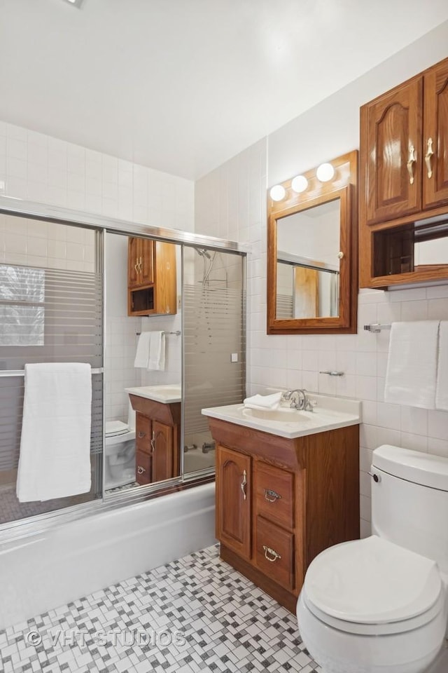 full bathroom featuring bath / shower combo with glass door, tile walls, tile patterned flooring, vanity, and toilet