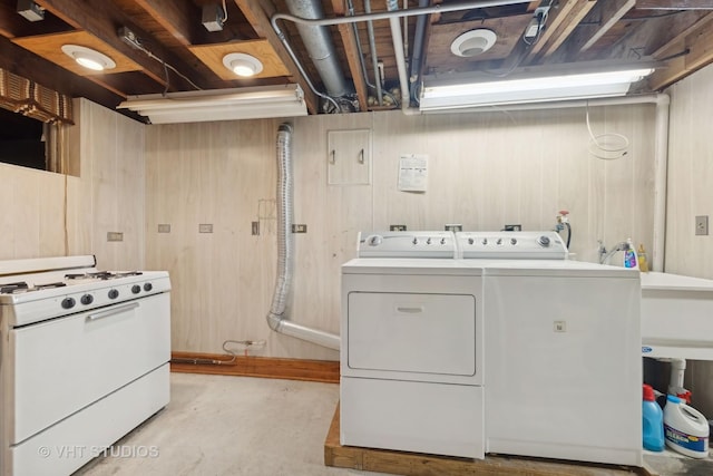 clothes washing area with washer and clothes dryer and wood walls