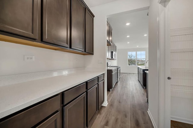 kitchen with light stone counters, dark brown cabinetry, and light hardwood / wood-style floors