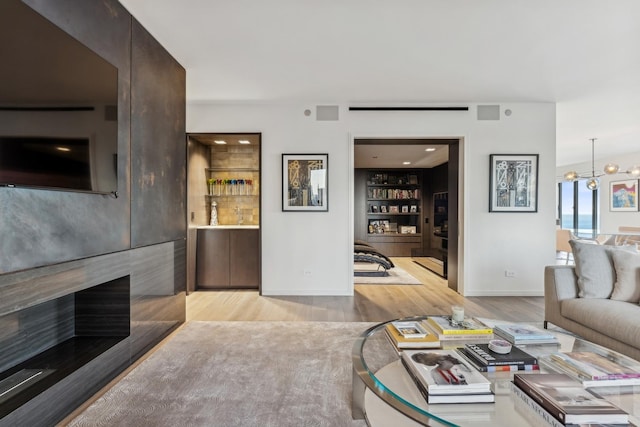 living room featuring a large fireplace, light hardwood / wood-style flooring, built in features, and a notable chandelier