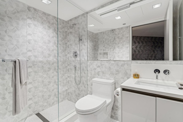 bathroom with tile walls, vanity, toilet, and a tile shower