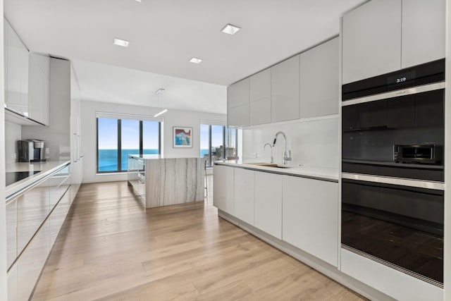 kitchen featuring sink, white cabinets, hanging light fixtures, light hardwood / wood-style floors, and a water view