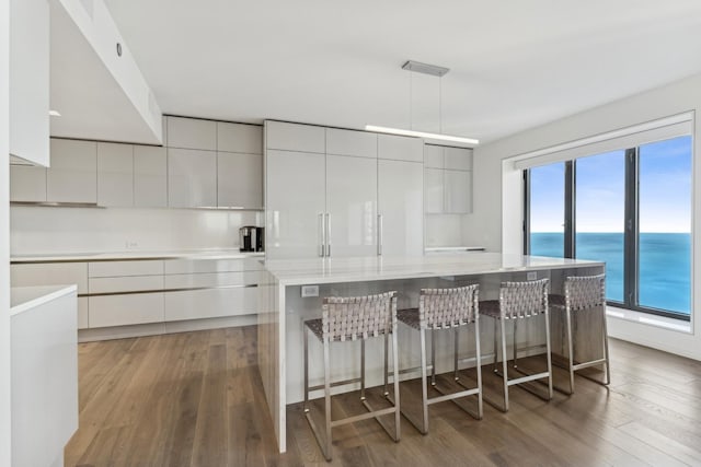 kitchen with a breakfast bar, a water view, decorative light fixtures, a kitchen island, and hardwood / wood-style floors