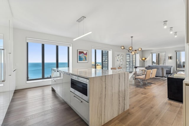 kitchen featuring a water view, a center island, pendant lighting, light stone countertops, and white cabinets