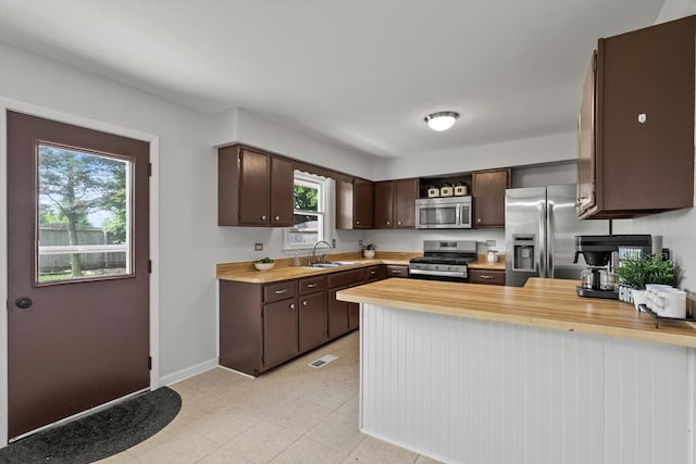 kitchen featuring stainless steel appliances, dark brown cabinets, a sink, a peninsula, and baseboards