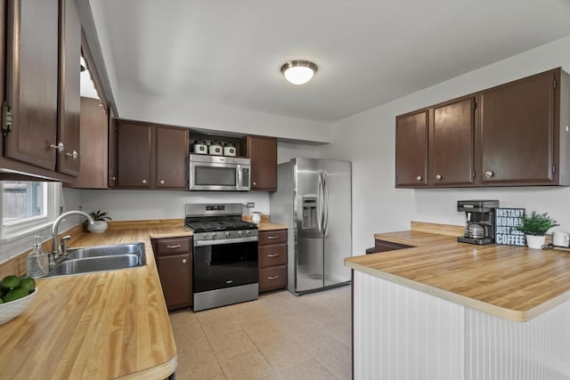 kitchen with appliances with stainless steel finishes, a sink, butcher block countertops, dark brown cabinets, and open shelves